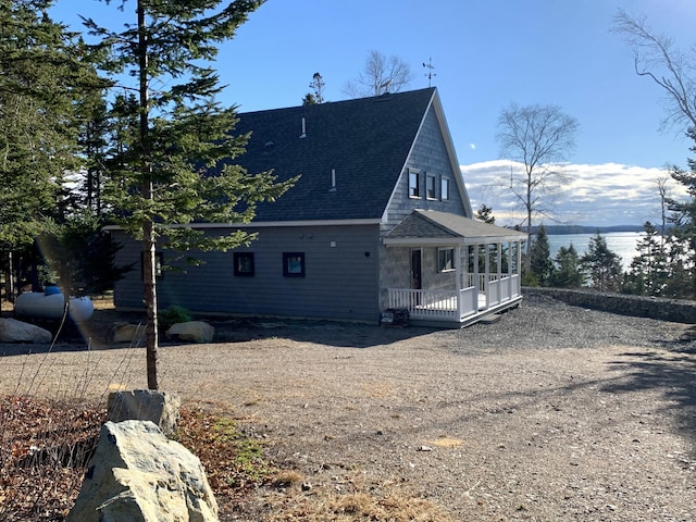 view of side of home featuring driveway, a shingled roof, and a porch