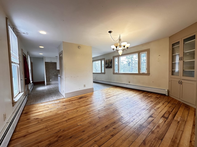 empty room featuring wood-type flooring, baseboard heating, and a chandelier