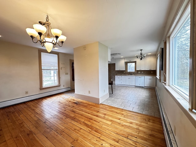 unfurnished living room with a healthy amount of sunlight, light tile floors, a baseboard heating unit, and an inviting chandelier