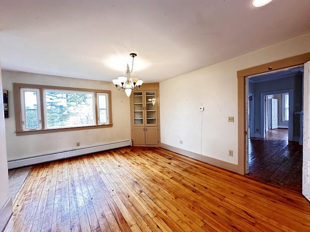 spare room featuring hardwood / wood-style flooring, an inviting chandelier, and a baseboard heating unit