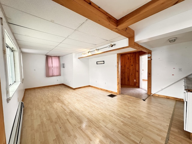 unfurnished living room featuring a drop ceiling, baseboard heating, wooden walls, and light wood-type flooring