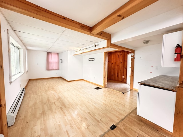 interior space featuring a drop ceiling, baseboard heating, and light hardwood / wood-style floors