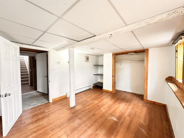 basement with a drop ceiling, light hardwood / wood-style flooring, and a baseboard radiator