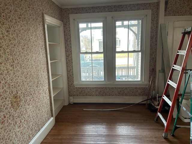 spare room featuring dark hardwood / wood-style floors, baseboard heating, and crown molding