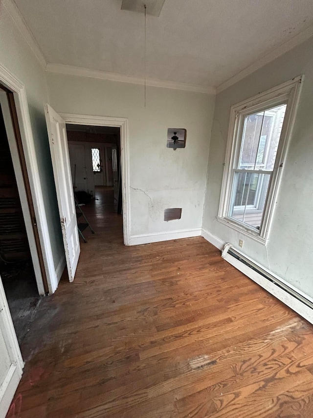 empty room featuring dark hardwood / wood-style floors, baseboard heating, and ornamental molding