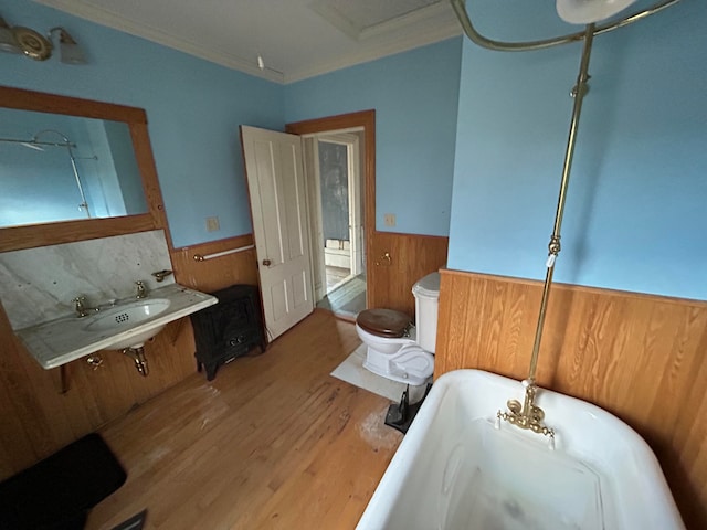 bathroom featuring ornamental molding, toilet, wooden walls, a bathtub, and hardwood / wood-style flooring