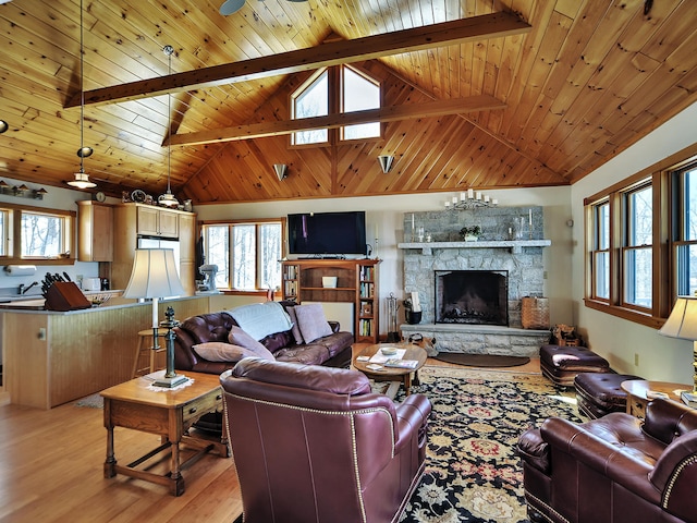 living room with beamed ceiling, light hardwood / wood-style floors, a stone fireplace, and wood ceiling