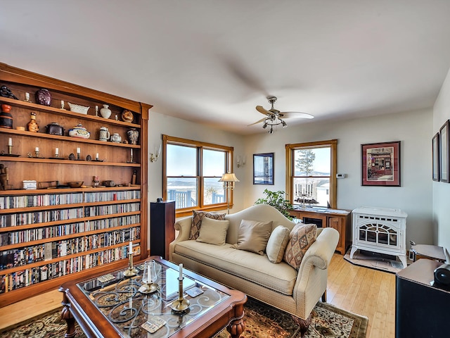 living room featuring ceiling fan, a healthy amount of sunlight, light wood-type flooring, and a wood stove