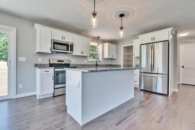 kitchen with pendant lighting, stainless steel appliances, white cabinetry, and light hardwood / wood-style flooring