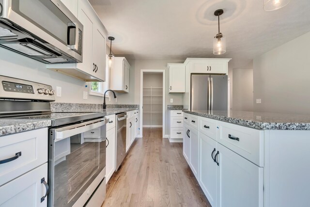 kitchen with appliances with stainless steel finishes, white cabinetry, decorative light fixtures, light hardwood / wood-style flooring, and light stone countertops