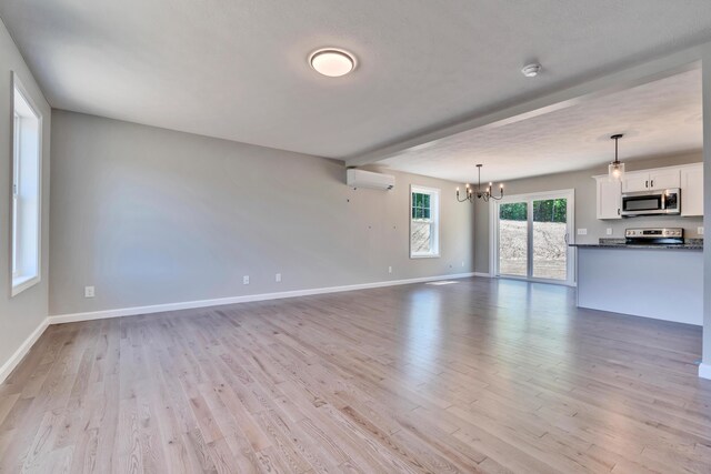 unfurnished living room featuring a wall unit AC, an inviting chandelier, and light wood-type flooring