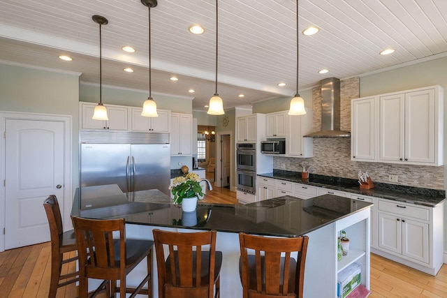 kitchen featuring pendant lighting, stainless steel appliances, dark countertops, white cabinets, and wall chimney range hood