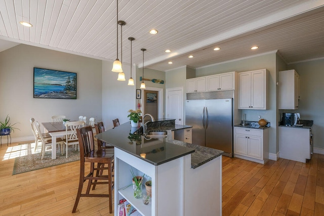 kitchen with light wood-style flooring, a kitchen island with sink, built in refrigerator, white cabinets, and pendant lighting