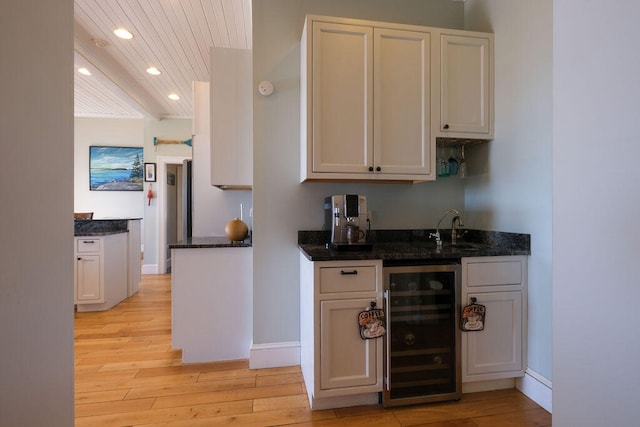 kitchen with beverage cooler, light wood finished floors, dark stone counters, and white cabinets