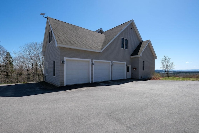 view of side of property featuring driveway, a shingled roof, and fence