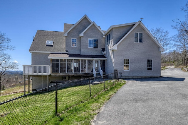 view of front of house with roof with shingles, a front yard, a sunroom, fence, and driveway