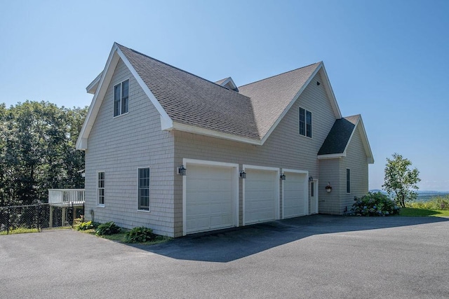 view of side of home with aphalt driveway, roof with shingles, and an attached garage