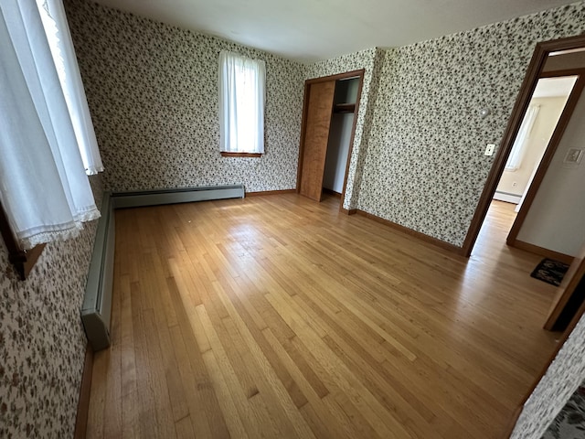 unfurnished bedroom with baseboard heating and light wood-type flooring