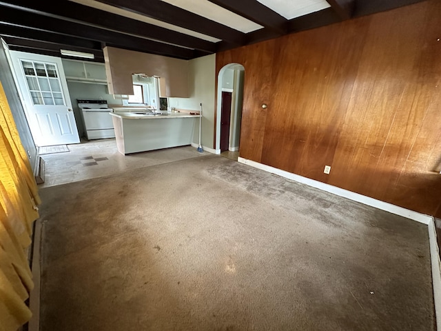 unfurnished living room with concrete floors, sink, wood walls, and beamed ceiling