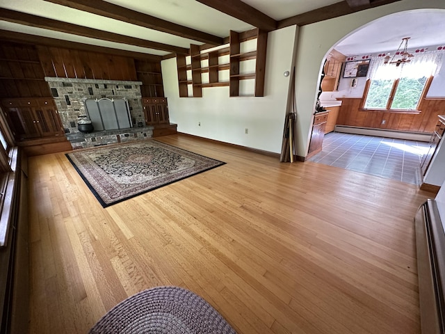 living room featuring a baseboard heating unit, beamed ceiling, wooden walls, light wood-type flooring, and a stone fireplace