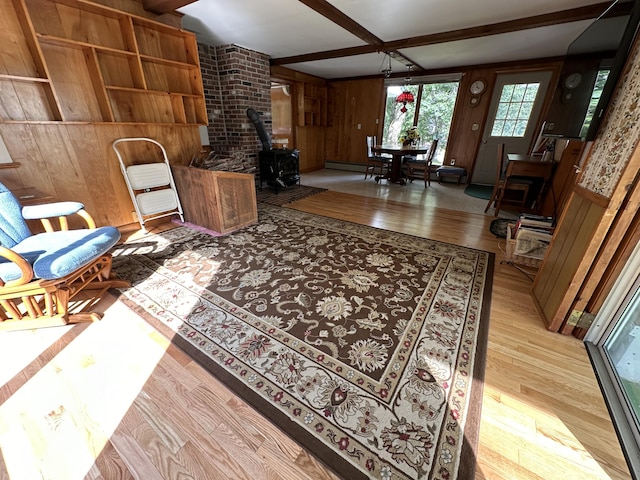 living room with wood walls, a wood stove, baseboard heating, light hardwood / wood-style flooring, and beamed ceiling