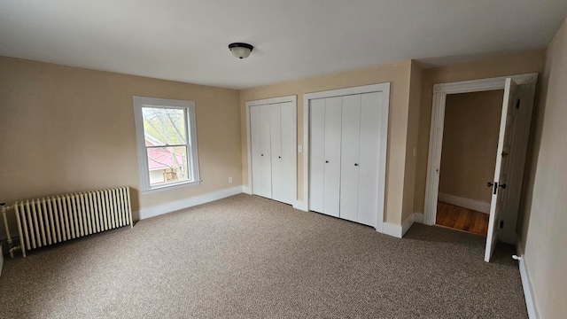 unfurnished bedroom with two closets, carpet flooring, and radiator heating unit