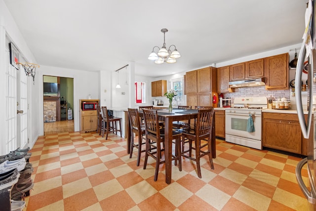 kitchen with black microwave, a notable chandelier, light tile floors, hanging light fixtures, and white gas stove