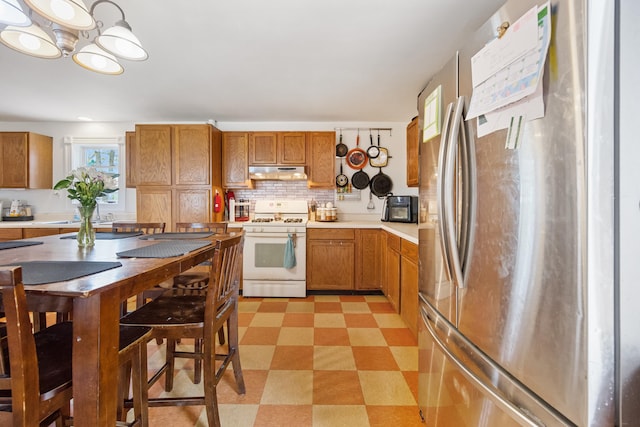 kitchen with an inviting chandelier, stainless steel refrigerator, gas range gas stove, tasteful backsplash, and light tile flooring