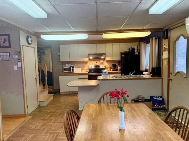 kitchen with stainless steel electric stove, light parquet flooring, a paneled ceiling, black fridge, and white cabinetry