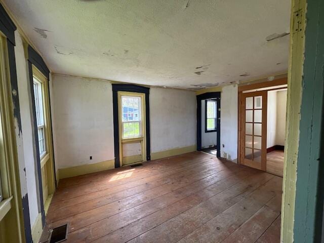 spare room with a textured ceiling, french doors, hardwood / wood-style floors, and a wealth of natural light