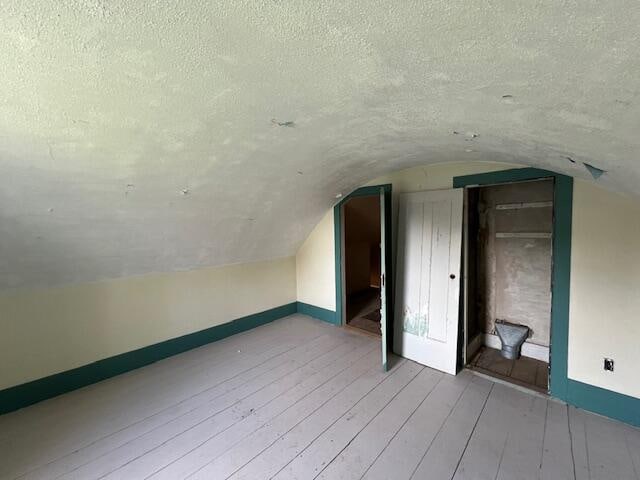 bonus room with wood-type flooring, a textured ceiling, and lofted ceiling