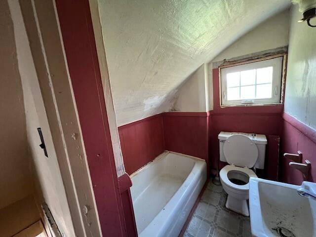 bathroom with tile flooring, lofted ceiling, and toilet