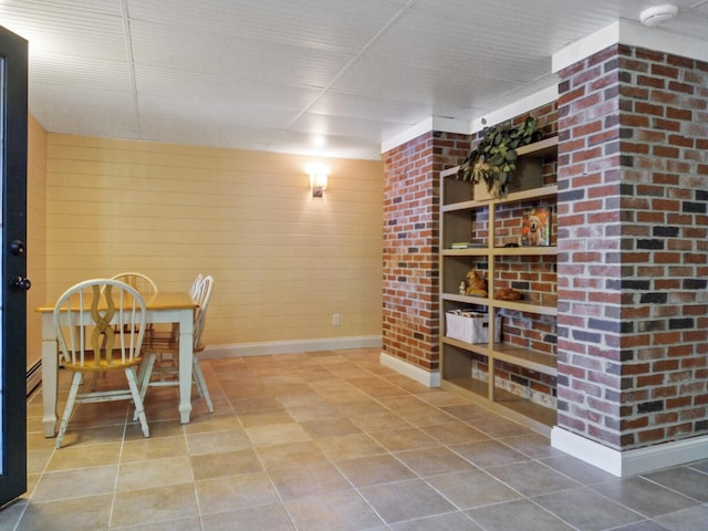 tiled dining space featuring wood walls, built in shelves, and baseboards