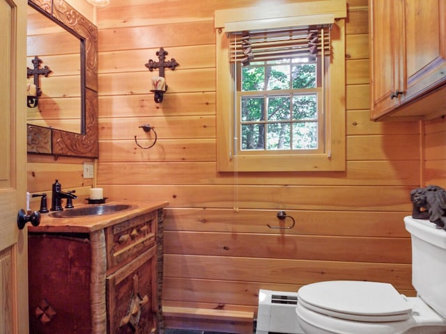 half bath with a baseboard heating unit, wood walls, vanity, and toilet