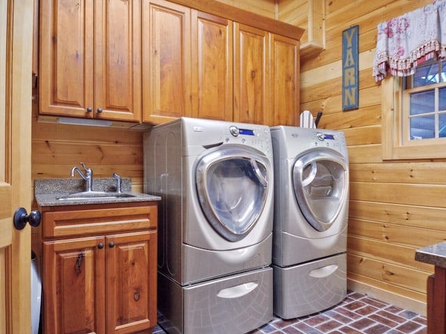 clothes washing area with cabinet space, washing machine and dryer, wooden walls, and a sink