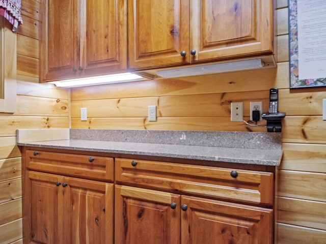 kitchen with wood walls, brown cabinetry, and light stone countertops