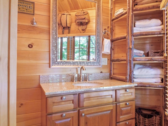 kitchen featuring a sink, wood walls, and light stone countertops