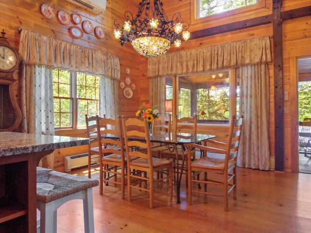 dining space featuring a chandelier, a baseboard heating unit, wood walls, wood finished floors, and an AC wall unit