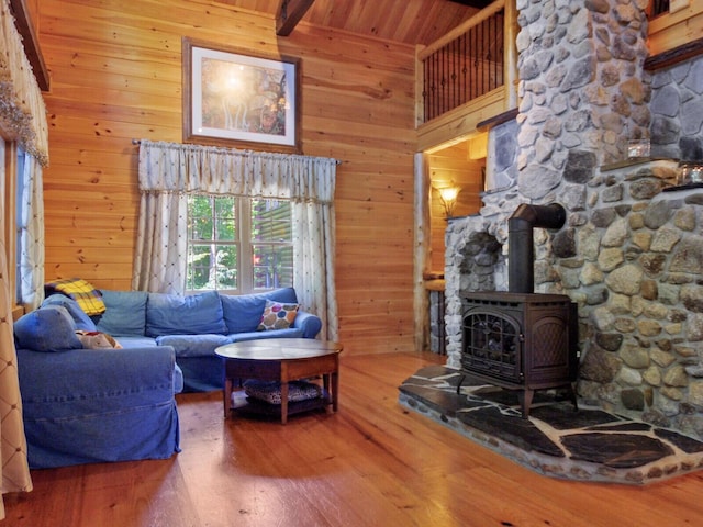 living room with wood walls, a towering ceiling, beam ceiling, hardwood / wood-style floors, and a wood stove