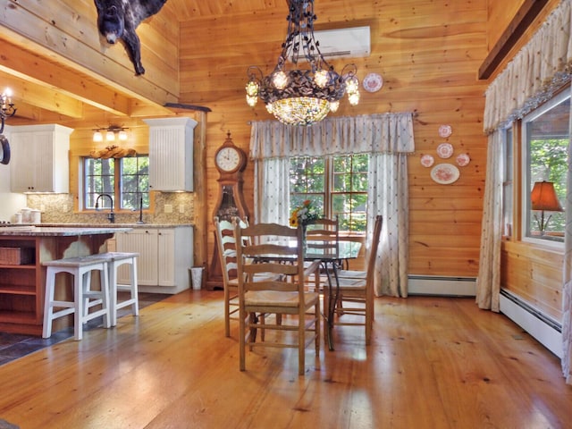 dining area featuring a notable chandelier, light wood finished floors, a baseboard radiator, and wooden walls