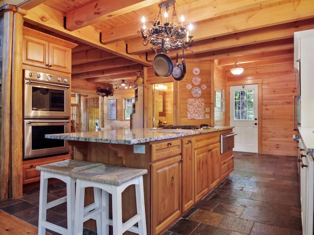 kitchen featuring beam ceiling, stone tile floors, stainless steel appliances, a kitchen island, and wooden walls