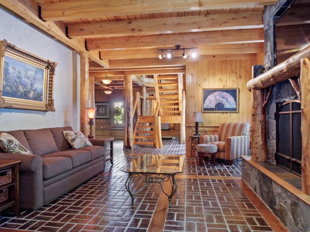 living room featuring beamed ceiling, stairway, brick floor, and wooden walls