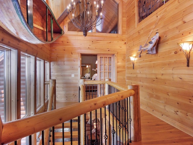 hallway featuring a towering ceiling, an upstairs landing, and wooden walls