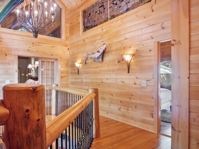 hall featuring wooden walls, wood finished floors, a towering ceiling, an upstairs landing, and an inviting chandelier