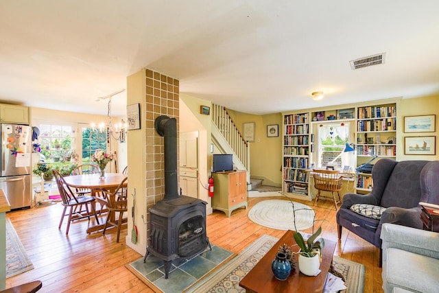 living room with rail lighting, a wood stove, an inviting chandelier, and light hardwood / wood-style floors