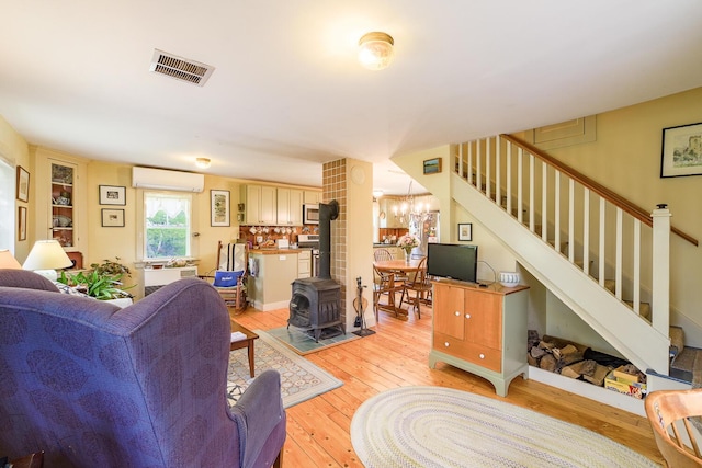 living room featuring a wall unit AC, light hardwood / wood-style floors, a chandelier, and a wood stove