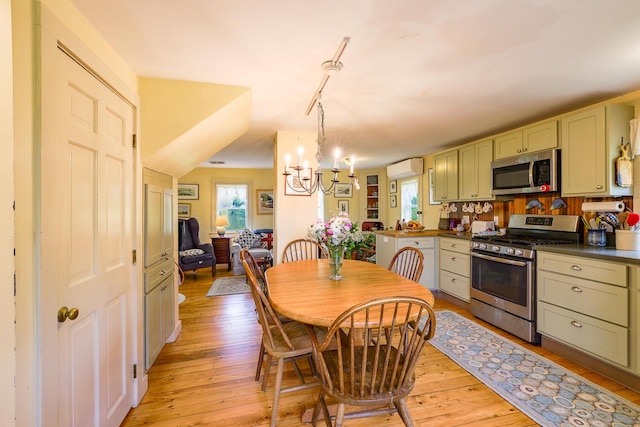 dining space with a wall mounted AC, a chandelier, track lighting, and light wood-type flooring