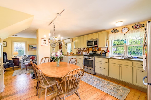 dining area with sink, light hardwood / wood-style flooring, track lighting, a wall unit AC, and a notable chandelier