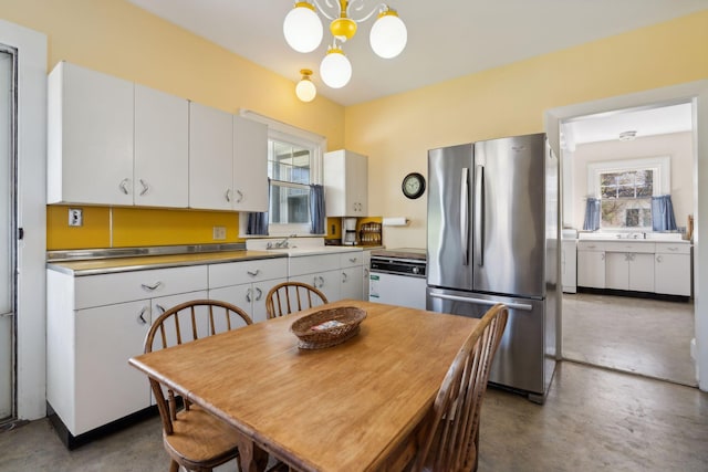 kitchen with stainless steel fridge, hanging light fixtures, white dishwasher, a notable chandelier, and white cabinets