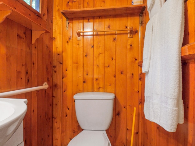 bathroom with sink, wood walls, and toilet